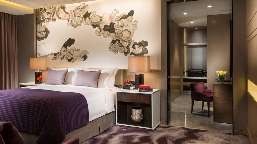 Executive Suite bed, nightstand, lamp under brushstroke mural, purple chair by desk