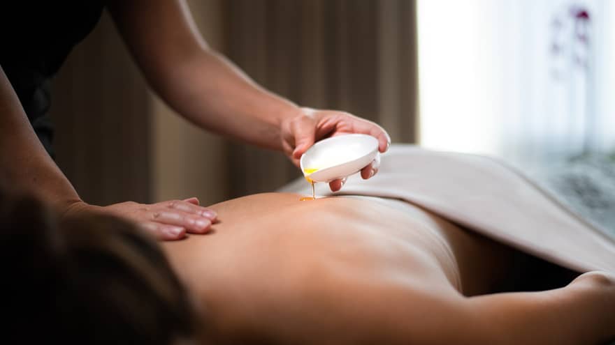 Spa staff pours hot oil on person's back during massage