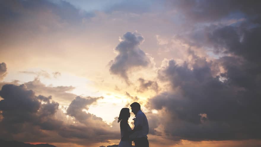 A silhouette of a man and woman embracing as the sun sets beyond them over the mountains