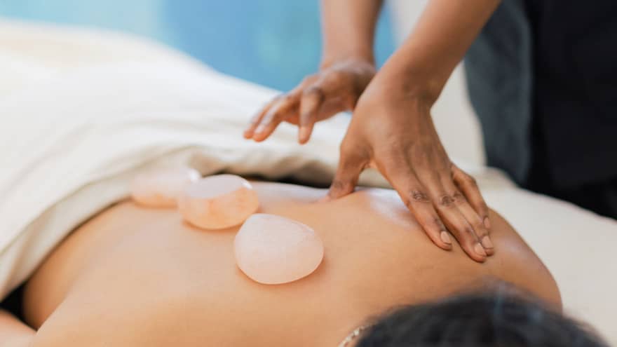 Masseuse places salt stones on a person's bare back