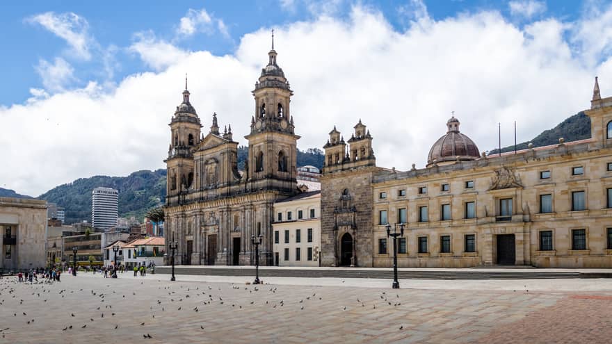 Exterior view of colonial-era La Catedral Primada with a brick plaza in the foreground and mountains in the background