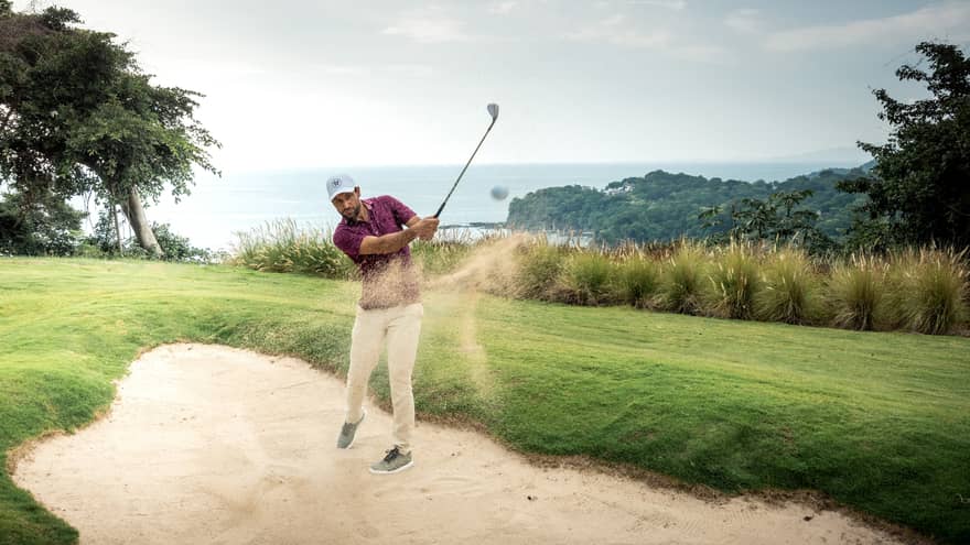 A golfer hitting a ball out of sand.