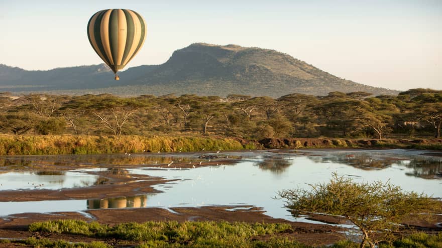 Striped hot air balloon floating over Serengeti fields, ponds