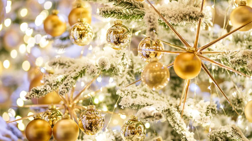 Several golden ornaments on a snow covered Christmas tree. 