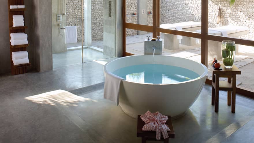 Tap running in Master Spa round freestanding tub by floor-to-ceiling window, glass shower