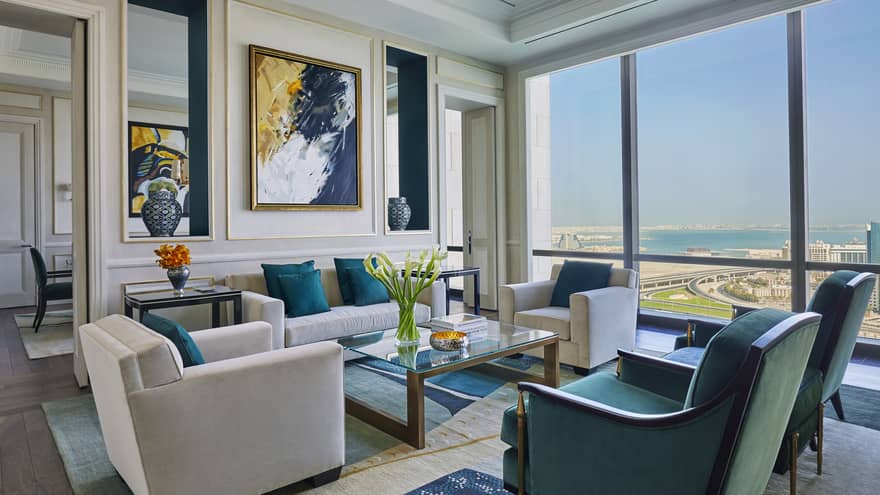 Hotel room living area with beige, green and gold seating area, modern art on wall, sunny windows