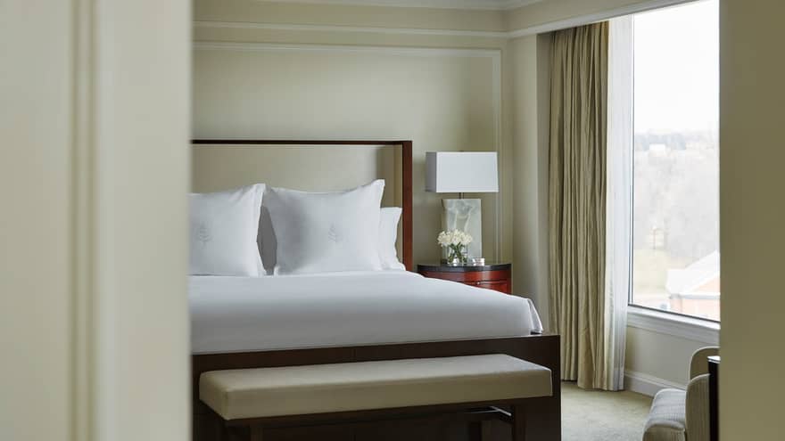 Presidential Suite west wing bed with white linens, white bench, sunny window through door frame