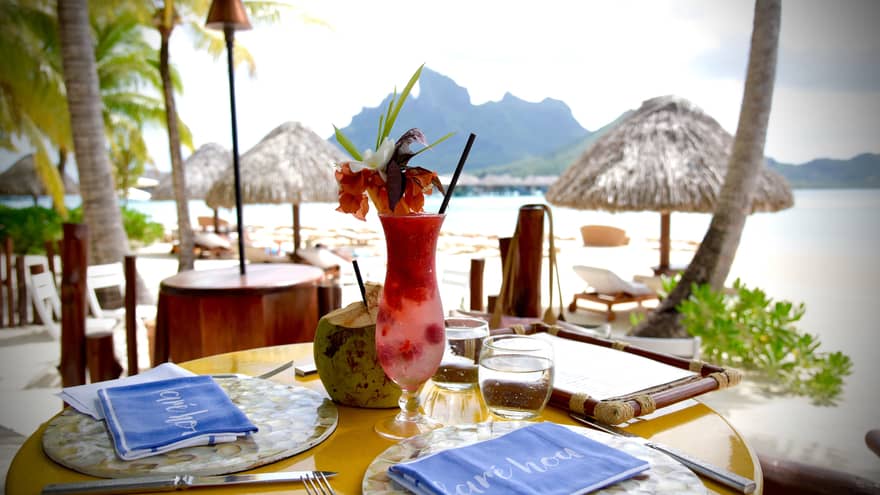 Fruity cocktail with tropical flower garnish on patio dining table by Bora Bora lagoon