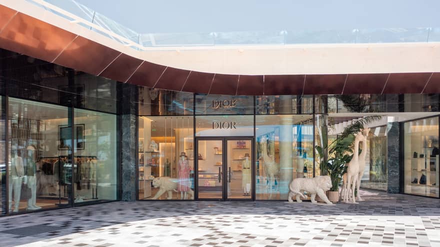 Exterior of glass-walled DIOR boutique with front door flanked by white lion statues