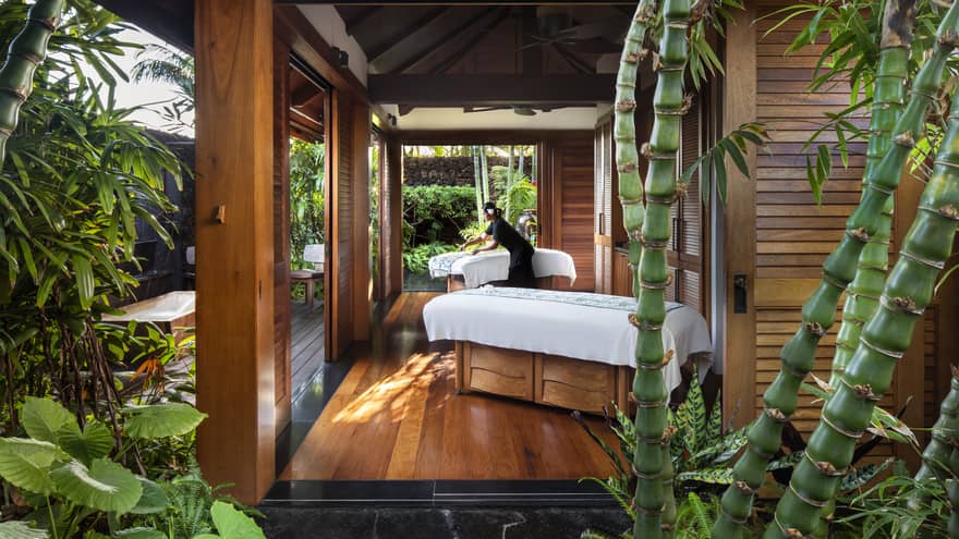 Spa staff spreads sheet on couples massage beds on open-air pavilion 