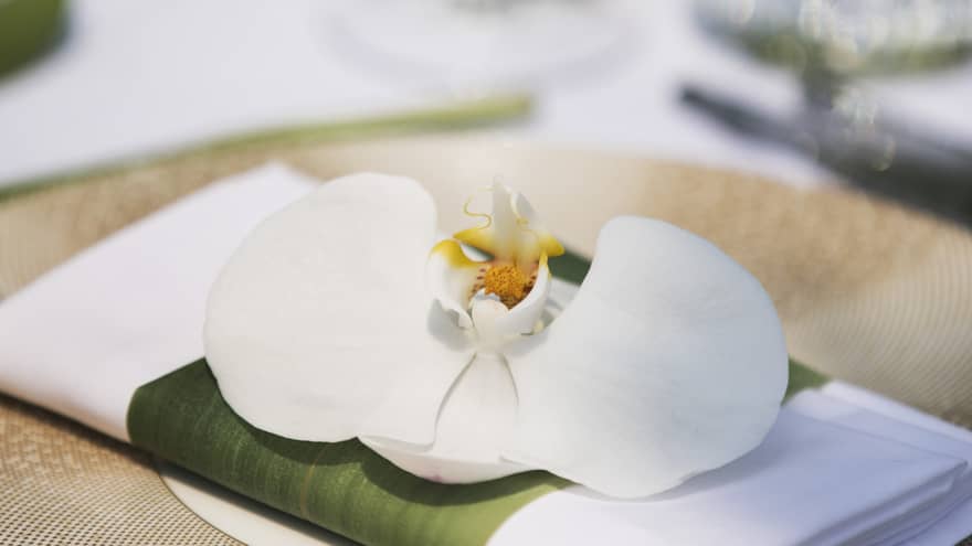A place setting of a gold charger with a white napkin and white lily on top of it at a Garden Buffet 