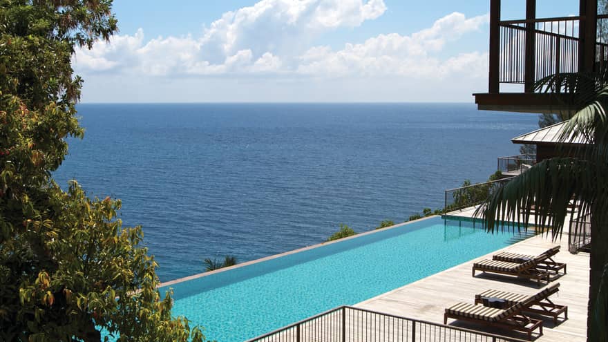 Long outdoor swimming pool on deck by lounge chairs under balcony, ocean views