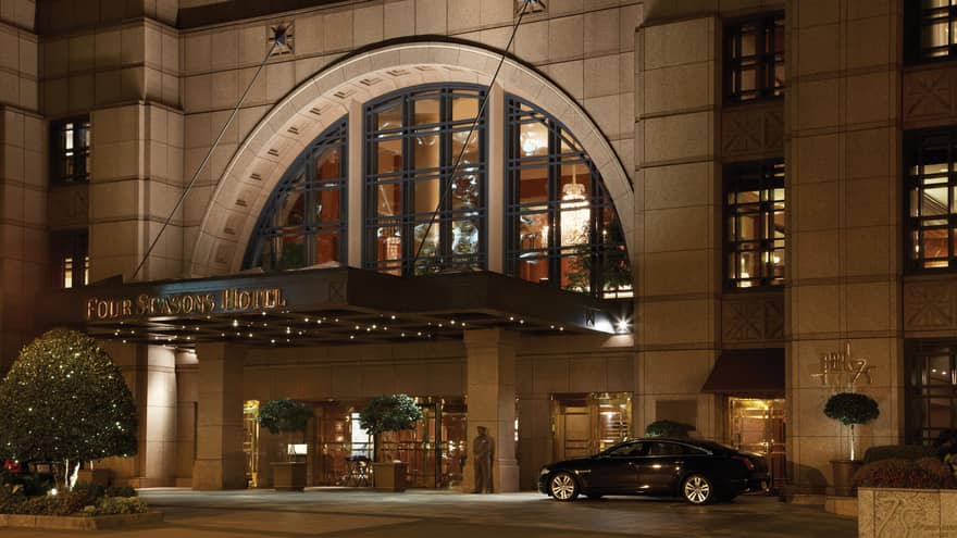 Black car beside arched doorway at front entrance, Four Seasons Hotel sign at night 