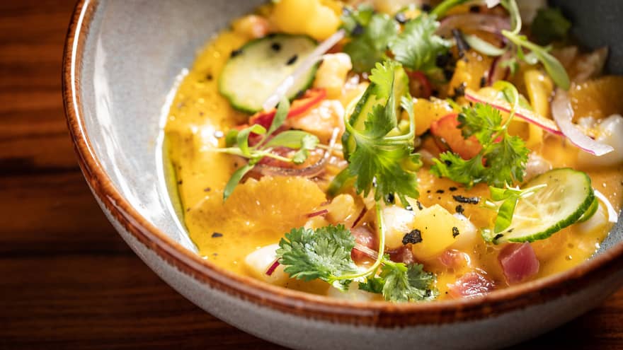 A bowl of yellow ceviche with scallops and shrimp garnished with citrus and cilantro.