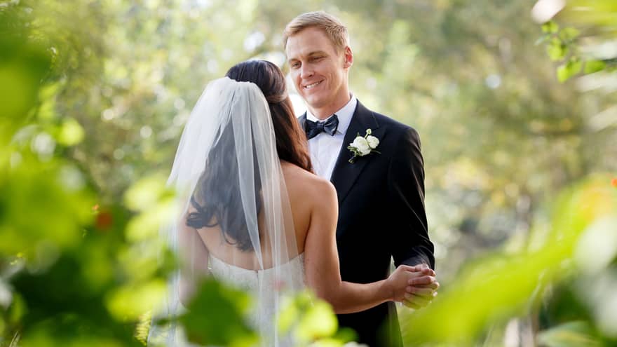 A person wearing a long veil dances joyfully with a smiling partner in a beautiful garden, surrounded by nature's splendor.