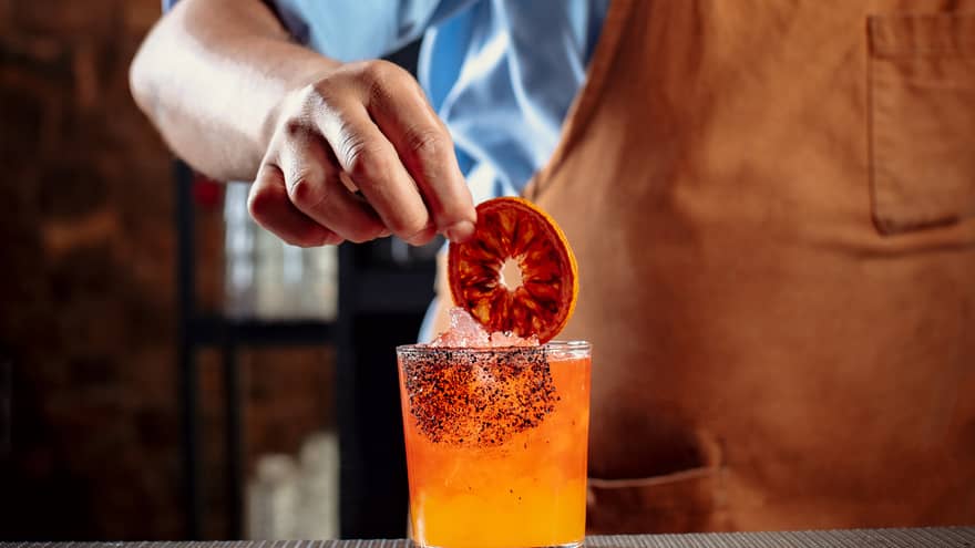 A bartender making an orange cocktail and putting a dark orange wheel in it.