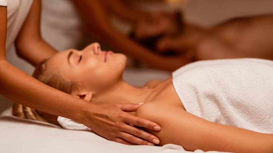 Two spa therapists perform a couples' massage