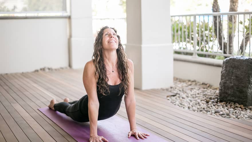 Woman smiles, looks up as she does yoga stretch on all fours on purple mat 