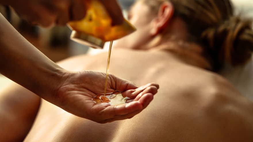 Person pouring oil into their hands while other person lies on spa table.