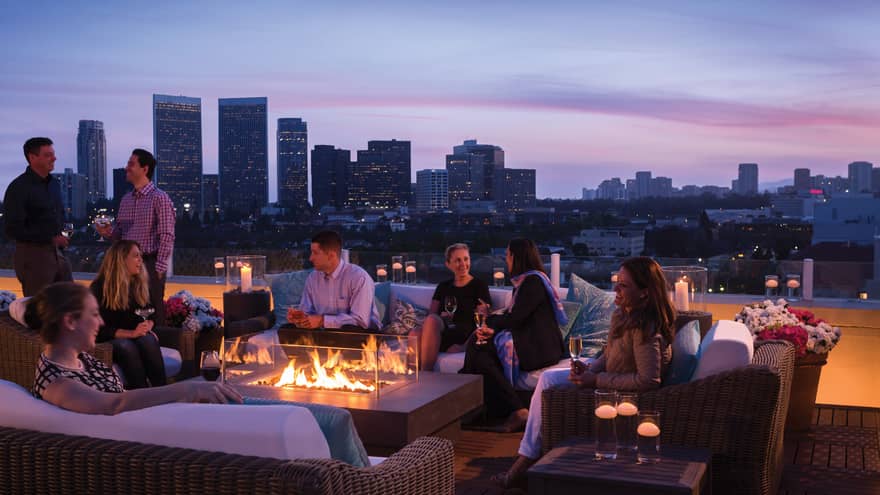 Guests socialize around outdoor fireplace Veranda Suite rooftop terrace, city views at dusk