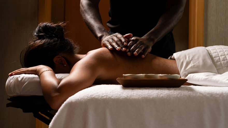 Masseur's hands rub oils on the bare back of a guest lying face down on a massage table