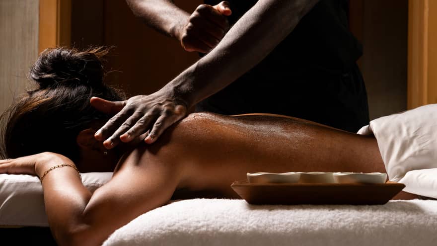 Woman gets a massage on a treatment table, with a wooden tray of ingredients nearby