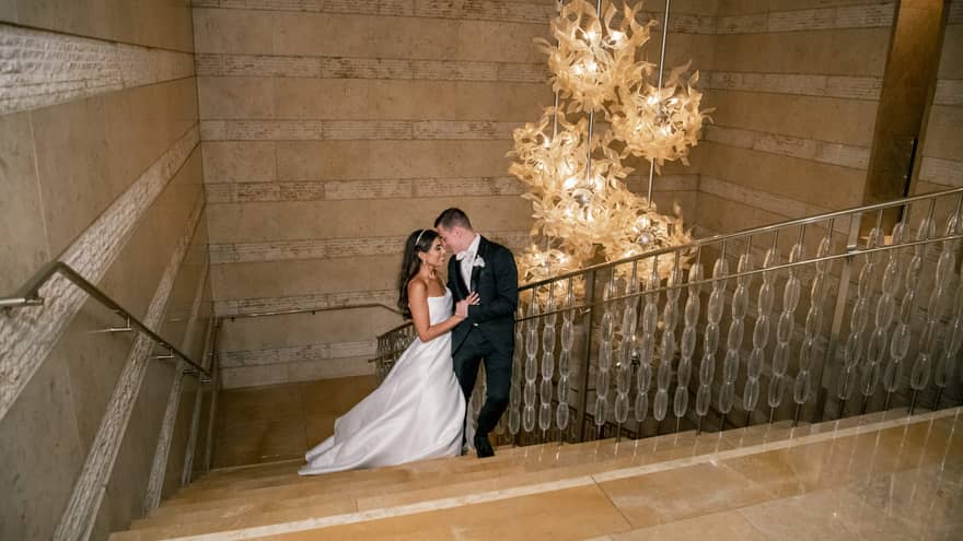 Two guests standing on a staircase, one wearing a wedding dress and the other wearing a tux
