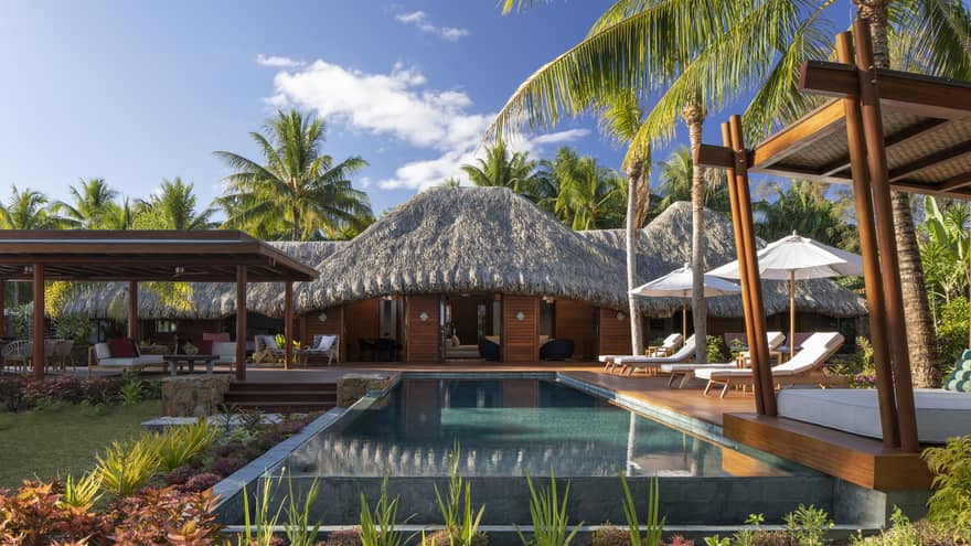 Private pool in a villa, with white sun chairs and a thatched-roof patio