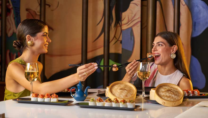 Two people enjoy dim sum with chopsticks from small bamboo steamer baskets are restaurant