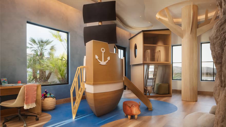 Children's playroom with a large-scale pirate ship play set, wooden tree, desk and climbing fort