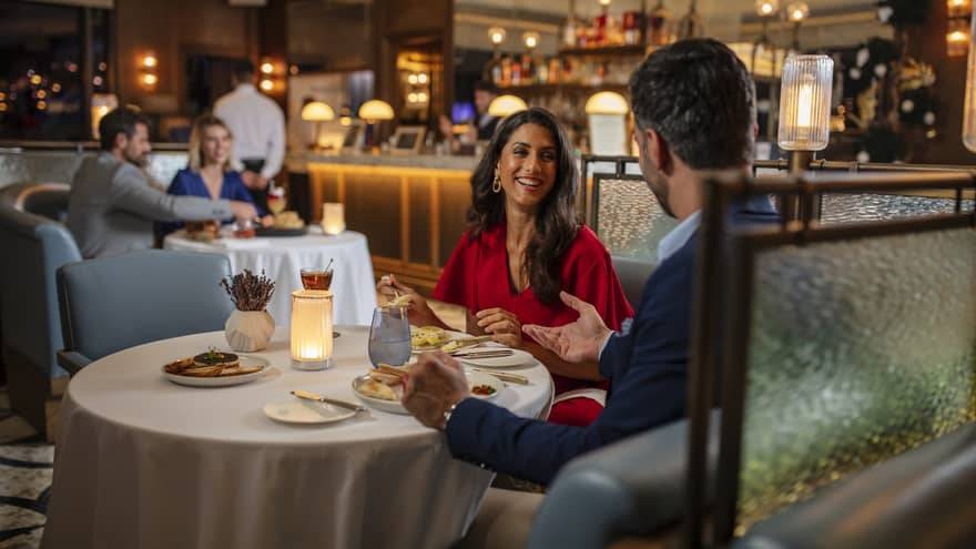 Woman in red dress, smiling at man, seated at round dining table in bar lounge