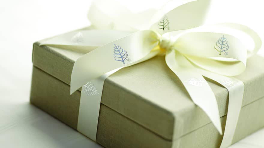 A tan gift box wrapped with ivory four seasons ribbon