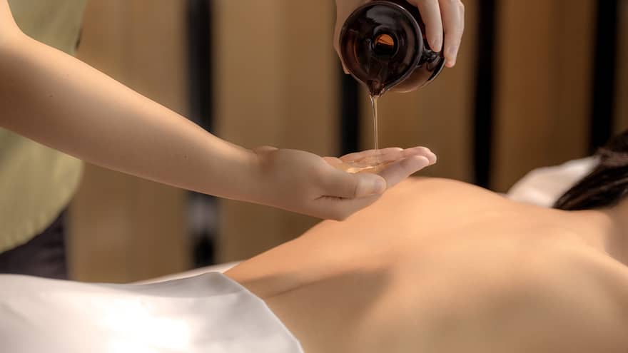 Spa therapist pours oil into hand above woman?s bare back in preparation for a massage