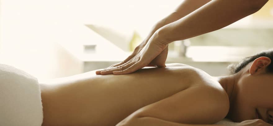 Masseuse reaches over, massages woman's bare back as she lies on spa table