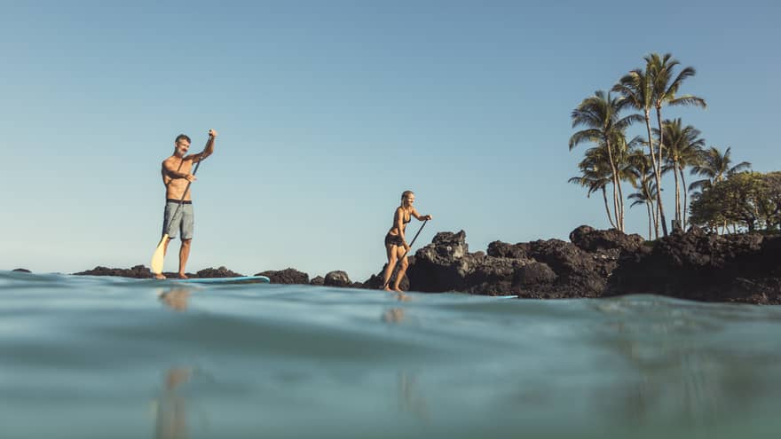 View from ocean looking up at two people on stand-up paddleboards near shore 