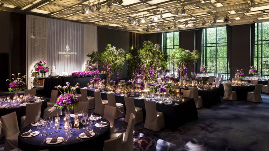 Elegant banquet hall at Four Seasons Hotel Kyoto with long tables set for a wedding reception, adorned with purple flowers and greenery.