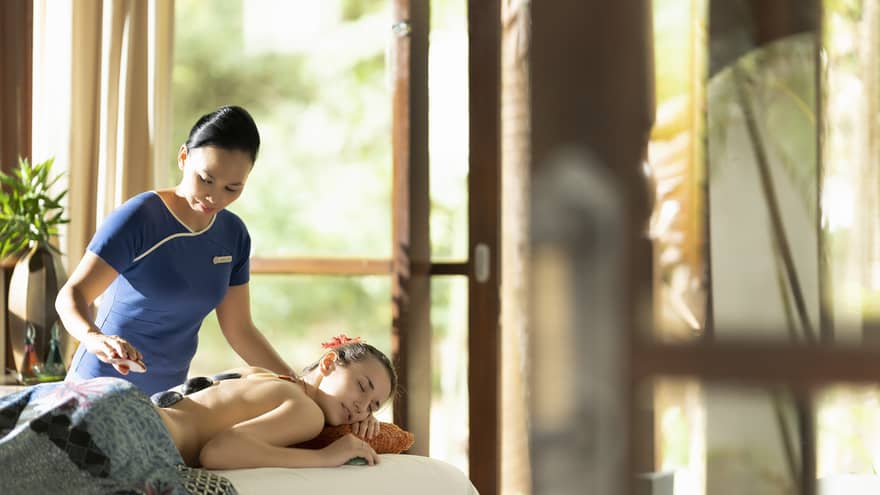 Massage therapist places hot stones along the spine of a guest during a treatment
