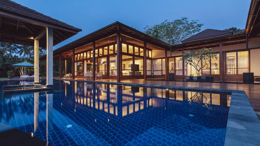 Pool with dark blue liner at dusk. Private villa is lit up in the background.