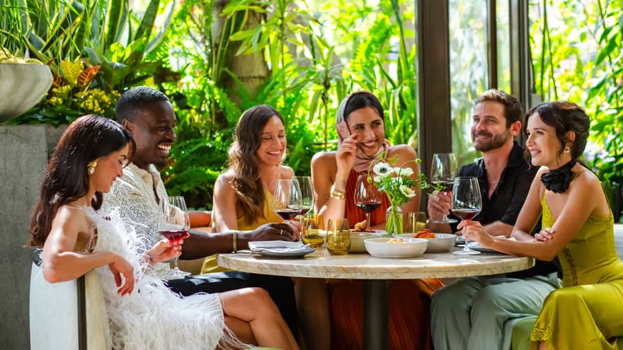 Group of friends dine together at round table at luxury hotel restaurant with greenery