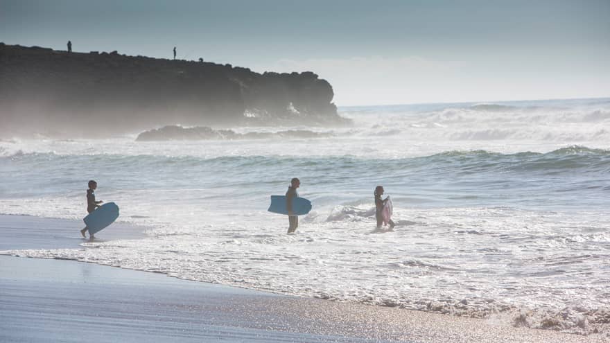 Silhouettes of man, woman and child all wearing wetsuits, holding blue surfboards, walking into ocean