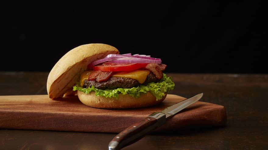 Cheeseburger sits on wooden cutting board with a knife