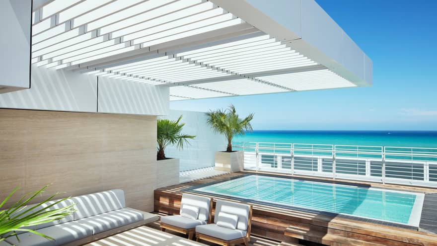 Outdoor covered patio with white furniture, beside small plunge pool, overlooking ocean