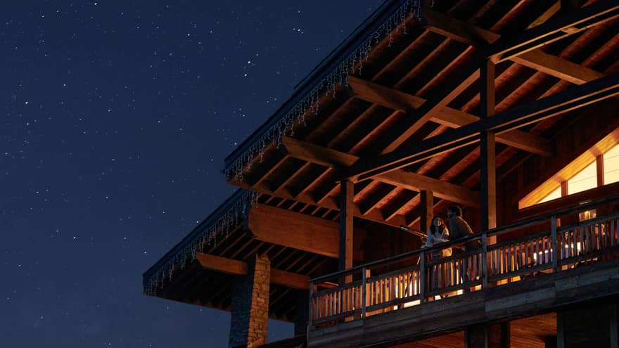 Couple standing on chalet balcony under vaulted ceiling and starry night sky