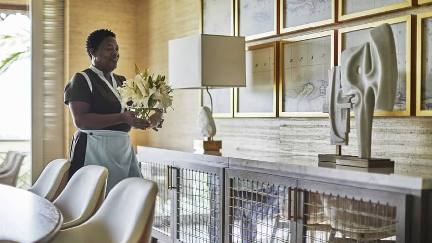 Housekeeping staff sets flower arrangement on dining room sideboard with lamp, modern sculpture