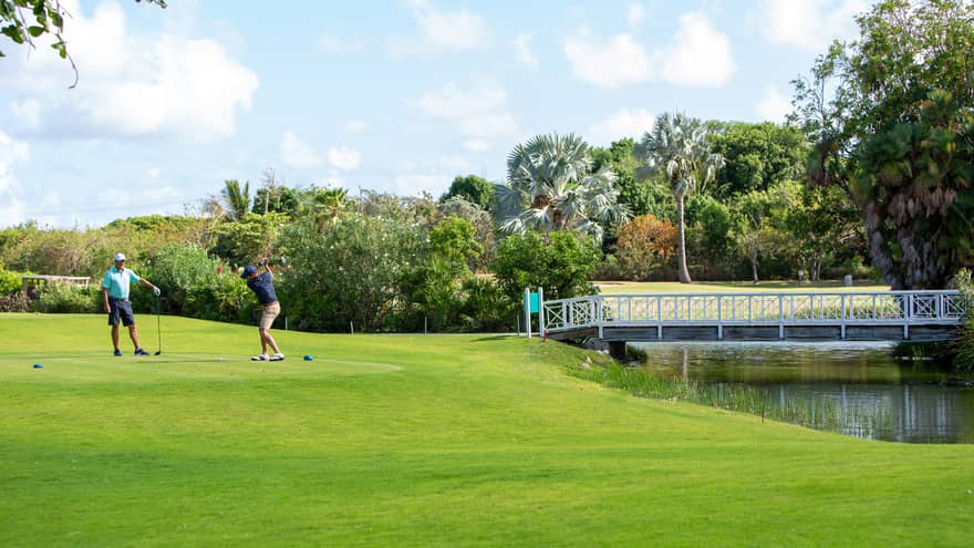 Two guests playing golf on a golf course near a lake and bridge