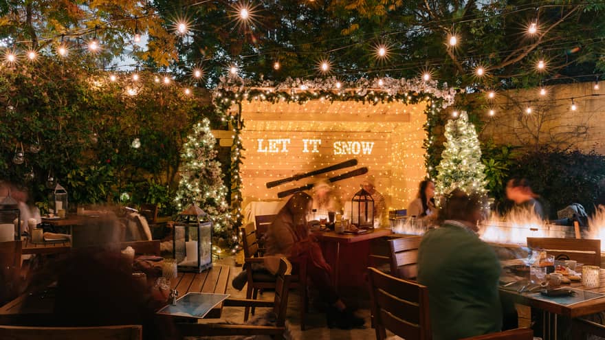 An outdoor seating area with people sitting by fires and Christmas lights.