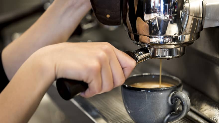 Close-up of hands pressing espresso in machine into small blue mug