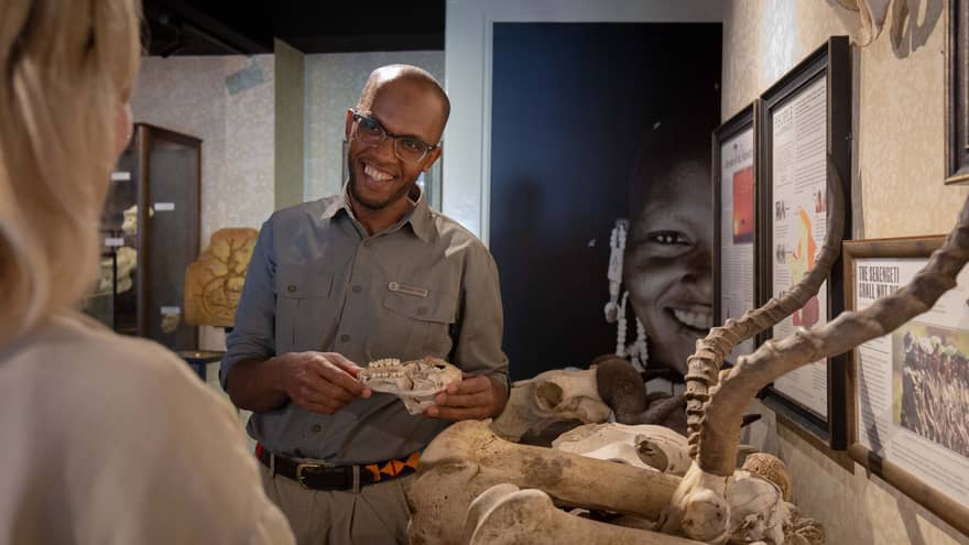 Person wearing glasses and park ranger?type shirt, smiling at person while holding a small animal skull