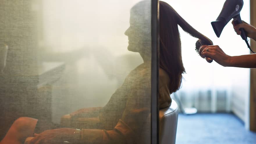 Silhouette of woman behind salon screen as hairdressers brushes, blow dries hair