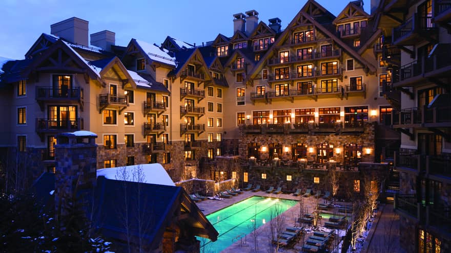 Four Seasons Vail hotel exterior at night with lit windows and balconies, glowing blue outdoor swimming pool